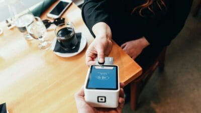 Osoba dokonująca płatności kartą w nowoczesnym terminalu płatniczym w restauracji lub kawiarni.