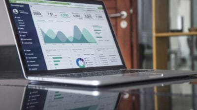 Laptop z otwartym panelem analitycznym, przedstawiającym wykresy finansowe i dane statystyczne w nowoczesnym biurowym otoczeniu.