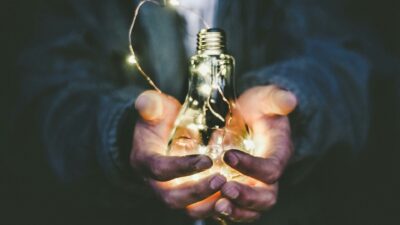 Osoba trzymająca żarówkę ozdobioną delikatnymi lampkami LED, symbolizująca oszczędność energii i efektywne zarządzanie zasobami.